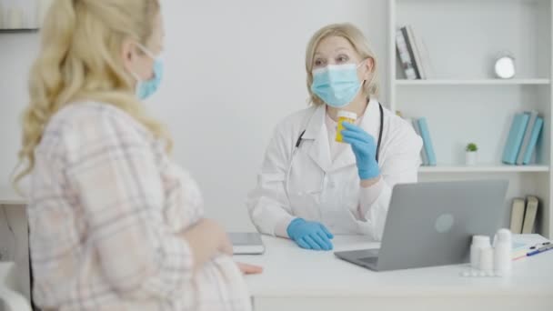 Ginekolog w masce pokazując pigułki do pacjenta, opieki prenatalnej podczas covid-19 — Wideo stockowe