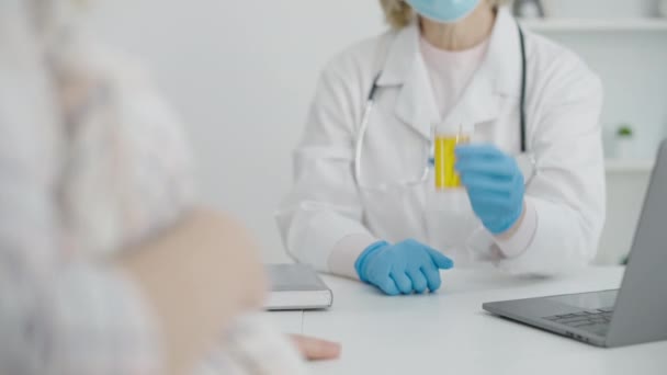 Lekarz w masce ochronnej i rękawiczki pokazujące butelkę tabletek do spodziewania się kobiety — Wideo stockowe