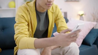 Neşeli, melez, gülümseyen genç bir erkek. Evdeki akıllı telefonlarda internet uygulaması kullanıyor.