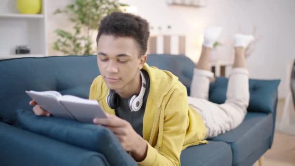 Relaxado Misto Raça Adolescente Cara Leitura Livro Sofá Casa Passatempo — Vídeo de Stock