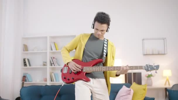 快乐的年轻人头戴耳机 喜欢在家里弹低音吉他手 玩得很开心 — 图库视频影像