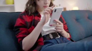 Evde akıllı telefondan sosyal medya uygulaması kullanan hevesli genç bir kadın.