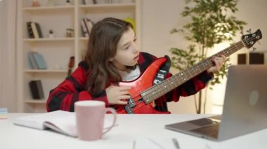 Gitar akorlarını öğrenen özenli bir kız dizüstü bilgisayar ve uygulama üzerinden ders izliyor.