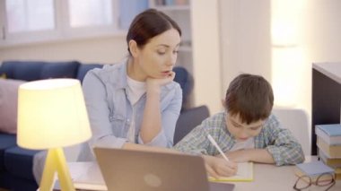 Karantina süresince oğlunun ödevlerini yapmasına yardım eden yorgun bir anne.