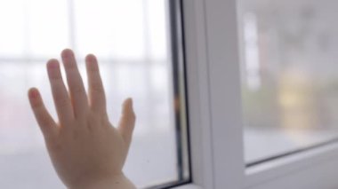 Koruyucu maskeli üzgün çocuk pencereden şehre bakıyor, kendini izole ediyor.