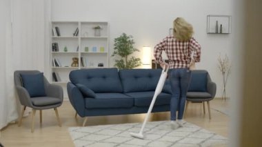 Oturma odasını elektrikli süpürgeyle temizlerken dans eden güzel genç bir kadın.