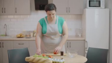 Genç bir kadın masada taze domates kesiyor, organik salata pişiriyor, diyet yapıyor.