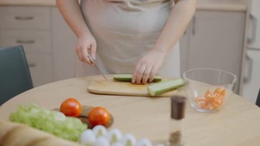 Ev hanımı organik salatalıkları kesiyor, vejetaryen salatası pişiriyor.