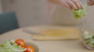 Marul parçalayan, cam kaseye koyan, taze sebze salatası pişiren bir kadın.