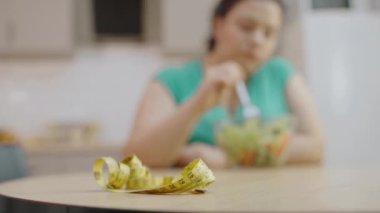 Masadaki bant ölçümü, arka planda salata yiyen kadın, kilo kontrolü.