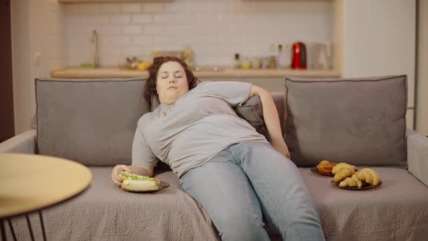懒洋洋的超重女人睡在家里的沙发上 夹着热狗和甜点 — 图库视频影像