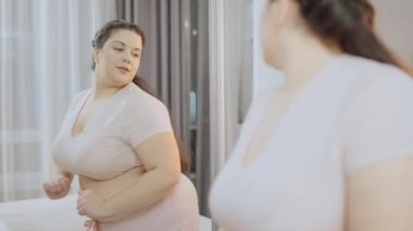 Gülümseyen artı boy kadın aynanın önünde dans ediyor, vücut pozitifliği, kendine güven