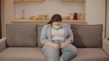 Maskeli genç obez kadın göbek yağına, karantina kilosuna ve vücut ağırlığına bakıyor.