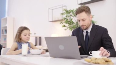 Üzgün küçük kız kendini yalnız hissediyor meşgul babaya bakıyor, dizüstü bilgisayarla evde çalışıyor.