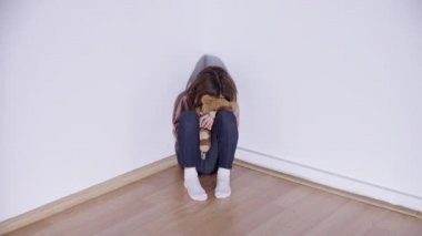 Yalnız ağlayan çocuk köşede oturuyor, oyuncak ayıya sarılıyor, aile sorunu var.