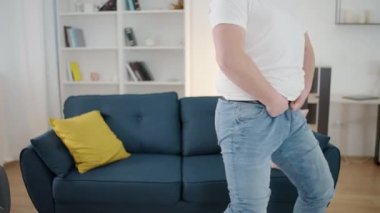 Kızgın obez adam evde dar pantolonları iliklemeye çalışıyor, artı boyut problemi.