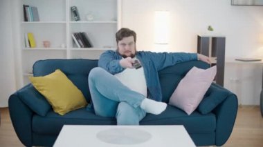 Genç tombul adam TV 'de kanal değiştiriyor, evde haberleri izliyor, eğleniyor.