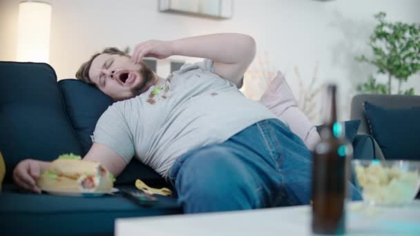 穿着肮脏衣服的懒惰肥胖单身汉睡在家里的沙发上吃热狗 — 图库视频影像