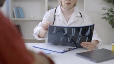 Fizyoterapist röntgen görüntülerini kontrol ediyor, hastaya yaralanma tedavisinde danışmanlık yapıyor.