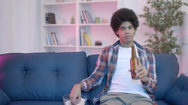 Junger Mann Sieht Fernsehsendung Allein Trinkt Bier Aus Flasche Isst — Stockvideo