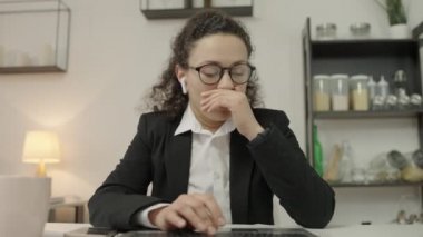 Çok çalışan iş kadını klavyede yazı yazıyor ve esniyor, fazladan çalışmaktan yorulmuş.