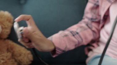 Çocuğun eli oyuncak ayıyla doktorculuk oynuyor, steteskopla oyuncakları inceliyor.