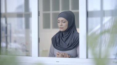 Üzüntülü, tesettürlü, pencereden dışarı bakan, depresyon ve yalnızlık hisseden Arap kadın.