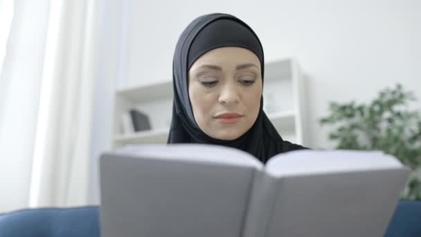 アラブ女性でスカーフ読書本でソファ 好きな趣味 リラクゼーション — ストック動画