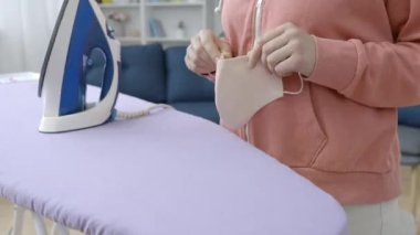 Çamaşır yıkama maskesinden sonra ütü yapan kadın. Salgın zamanı.