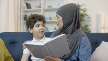 Önemseyen Müslüman anne küçük oğluna kitap okuyor, birlikte vakit geçiriyorlar, aile.