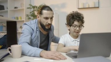 Tatmin olmuş baba ve oğul dizüstü bilgisayarla okul projesini bitiriyor ve beşlik çakıyor.