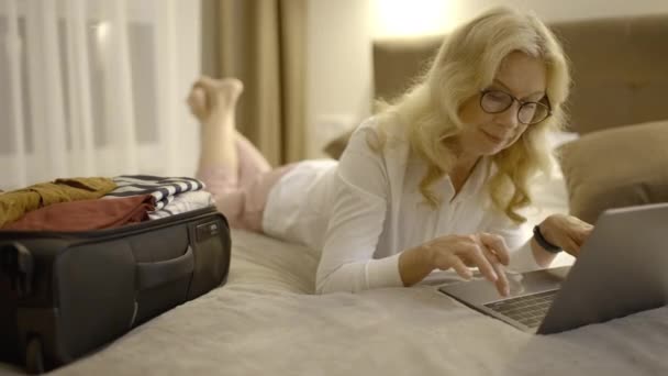中年の女性マネージャーは ラップトップで電子メールを送信し ホテルのベッドで働いています — ストック動画