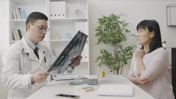 外傷外科医は 患者をチェックX線画像 診療所でアジアの女性に相談 — ストック動画