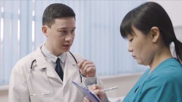 Seriöser asiatischer Arzt spricht mit Kollegin über Behandlungsplan, Teamwork