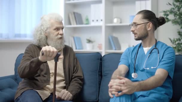 Hombre Mayor Hablando Con Médico Sentado Sofá Servicio Atención Domiciliaria — Vídeo de stock