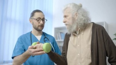 Rehabilitasyon uzmanı olgun bir adamın halterle egzersiz yapmasına yardım ediyor.