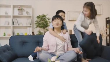 Rahat anne nilüferde meditasyon yapıyor kanepede poz veriyor, yaramaz çocuklar oynaşıyor.