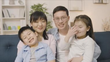 Kamerada gülümseyen ve sarılan Asyalı aile, aile ve iki çocuğun portresi.