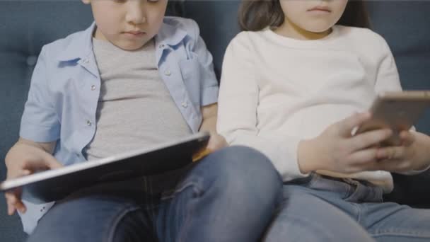Kleiner Junge Und Mädchen Auf Couch Mit Tablett Und Smartphone — Stockvideo