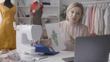 Kıyafet tasarımcısı internetten müşteriyle konuşuyor, elinde robot resim, teknoloji var.
