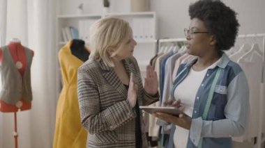 Kıyafet tasarımcısı müşteriyle konuşuyor, atölyede tablet üzerinde çalışıyor, terzilik yapıyor.