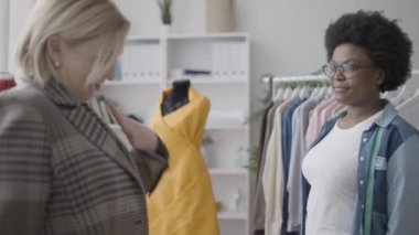 Moda stüdyosunda terzinin elini sıkan, kıyafet diken, serbest çalışan mutlu bir kadın.