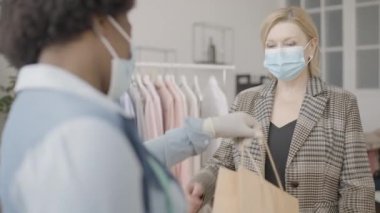 Koruyucu maske takan mutlu kadın sergi salonunda alışveriş çantası alıyor.