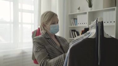 Sarışın, koruyucu maskeli bir kadın Covid-19 sırasında galeride kıyafet seçiyor.