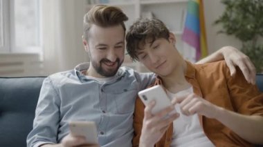 Aynı cinsiyetten çiftler, akıllı telefonlarıyla kanepede oturup birlikte vakit geçiriyorlar.