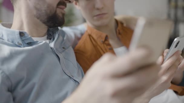 モバイルアプリを使ってスマートフォンをスクロールしている2人の男性の友人が — ストック動画
