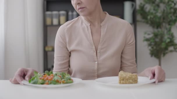 看着沙拉和蛋糕在健康饮食和不健康饮食之间做出选择的女人很不高兴 — 图库视频影像