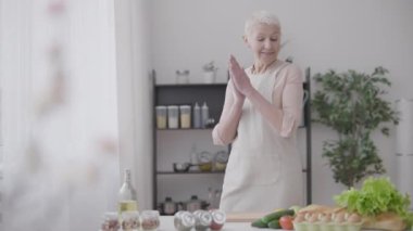 Mutfakta dans eden neşeli kadın ağır çekim, yemek pişirmekten hoşlanan olgun kadın.