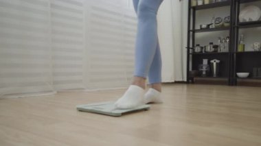 Zayıf, olgun bir kadın, terazinin üzerinde duruyor, tatlı pasta yiyor, kilo kontrolü yapıyor.