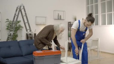 Tamirci kırık sandalyeyi tamir ediyor, yaşlı bir müşteri tarafından aceleye getirildiğini hissediyor.